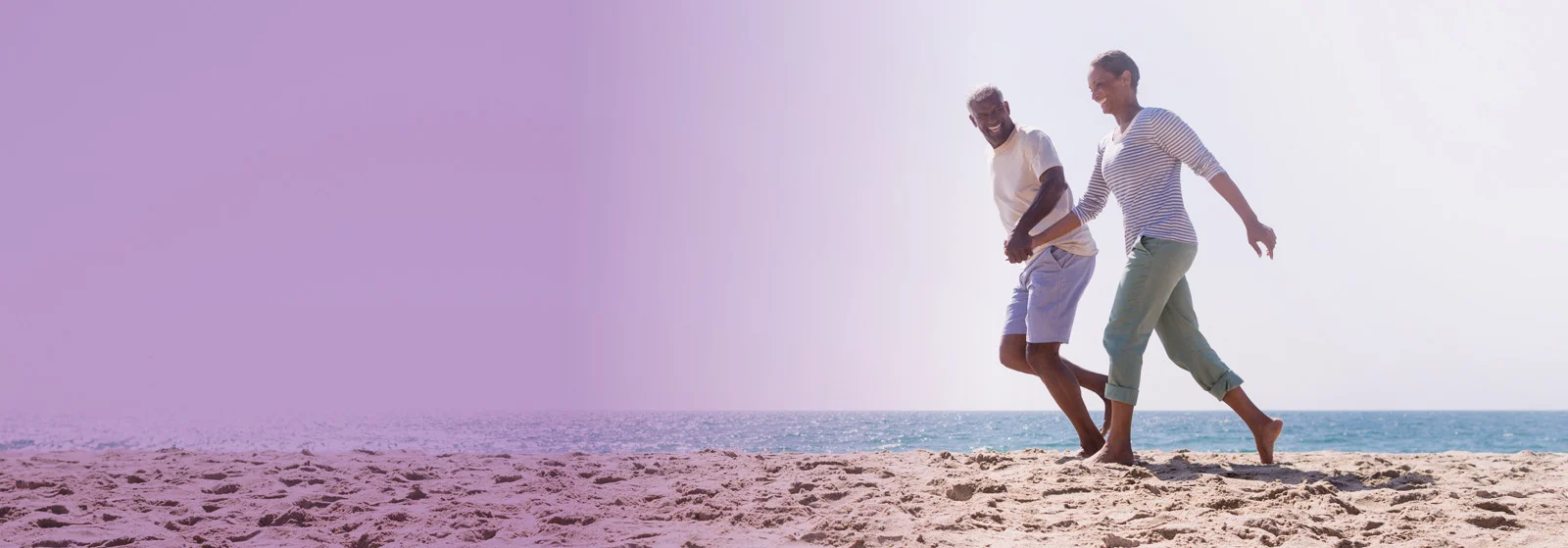 elderly couple holding hands on the beach and smiling