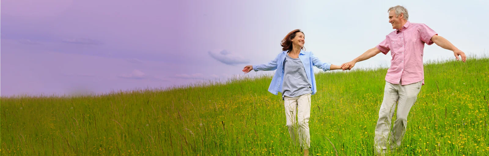 elderly couple holding hands in a field and smiling